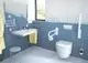 Bad mit blauen Fliesen und weißer Ideal Standard Sanitärkeramiken. Sichtbarer Waschtisch mit Armatur, Handtuchhalter und Toilette neben einem Fenster mit Tageslicht.